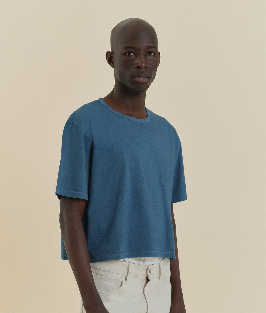 Portrait of a man wearing a blue t-shirt against a beige background - Industry of All Nations