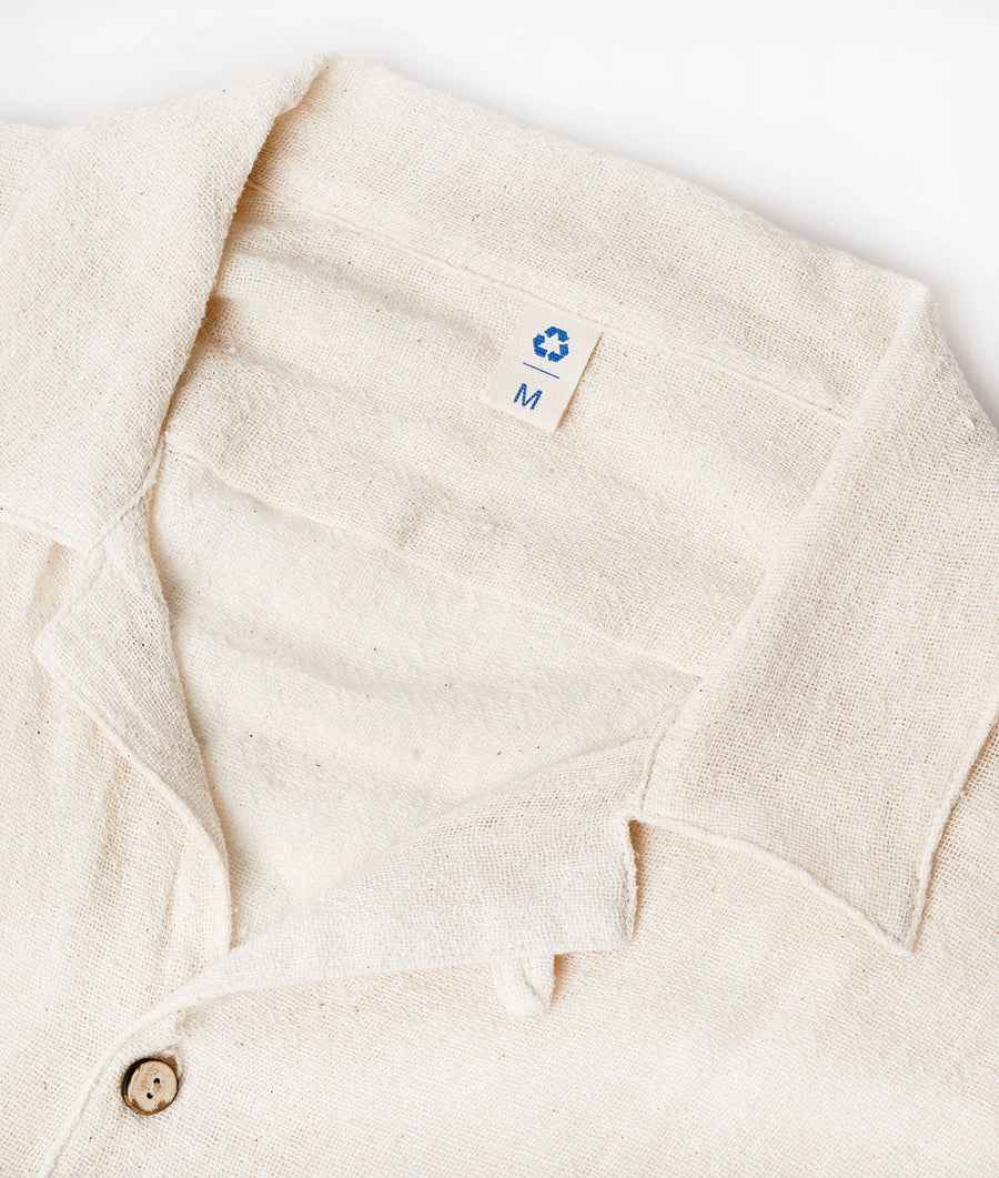 Flat lay shot of a cream-colored organic cotton jacket with recycling symbol and 'M' label - Industry of All Nations