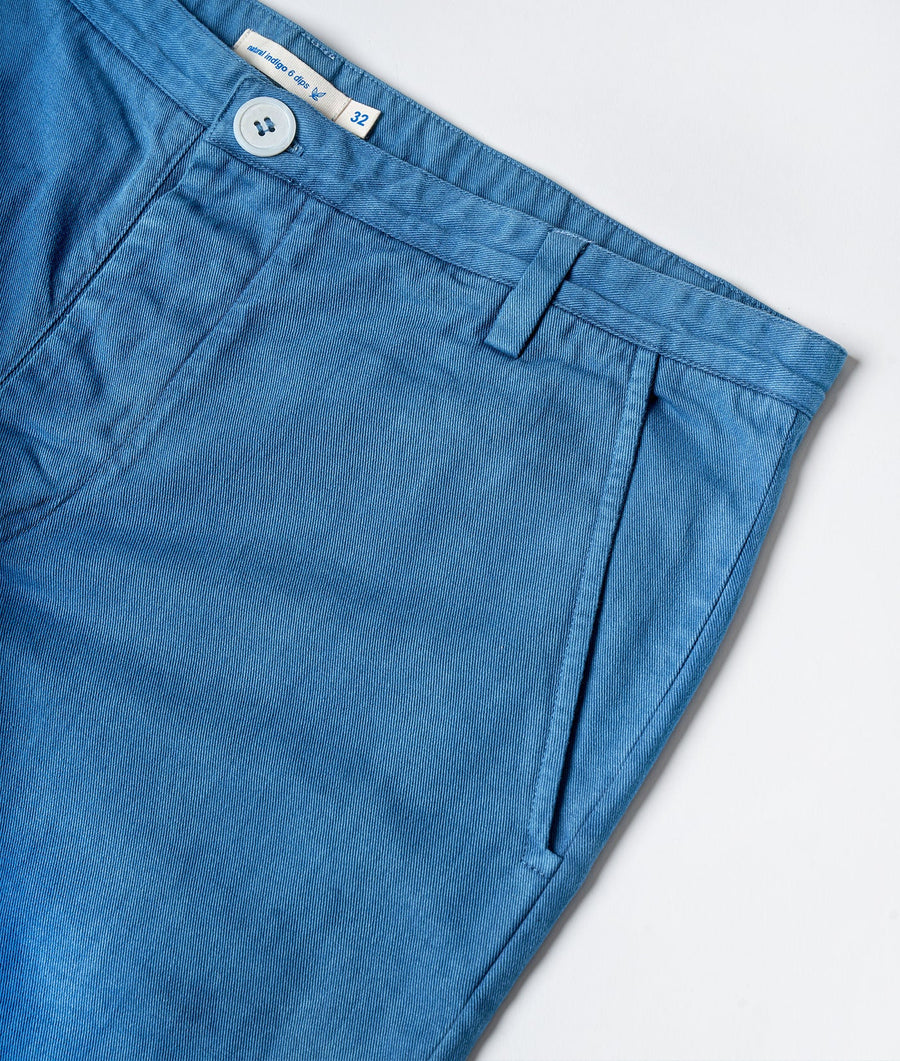 Close-up detail shot of a blue cotton denim men's pants with button closure, size tag and curved pockets - Industry of All Nations.
