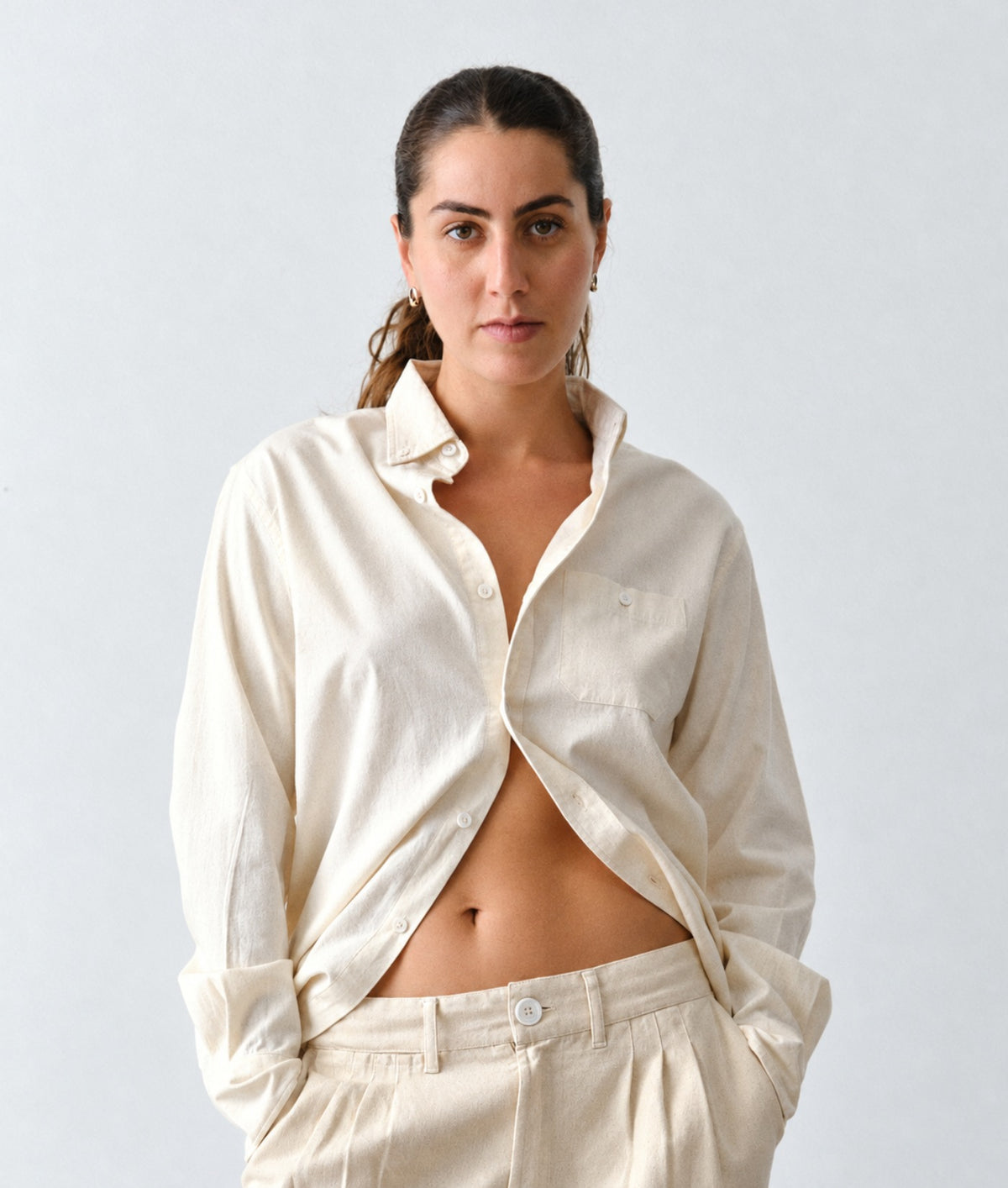A woman modeling IOAN undyed Madras shirt and matching trousers against a light gray studio background.
