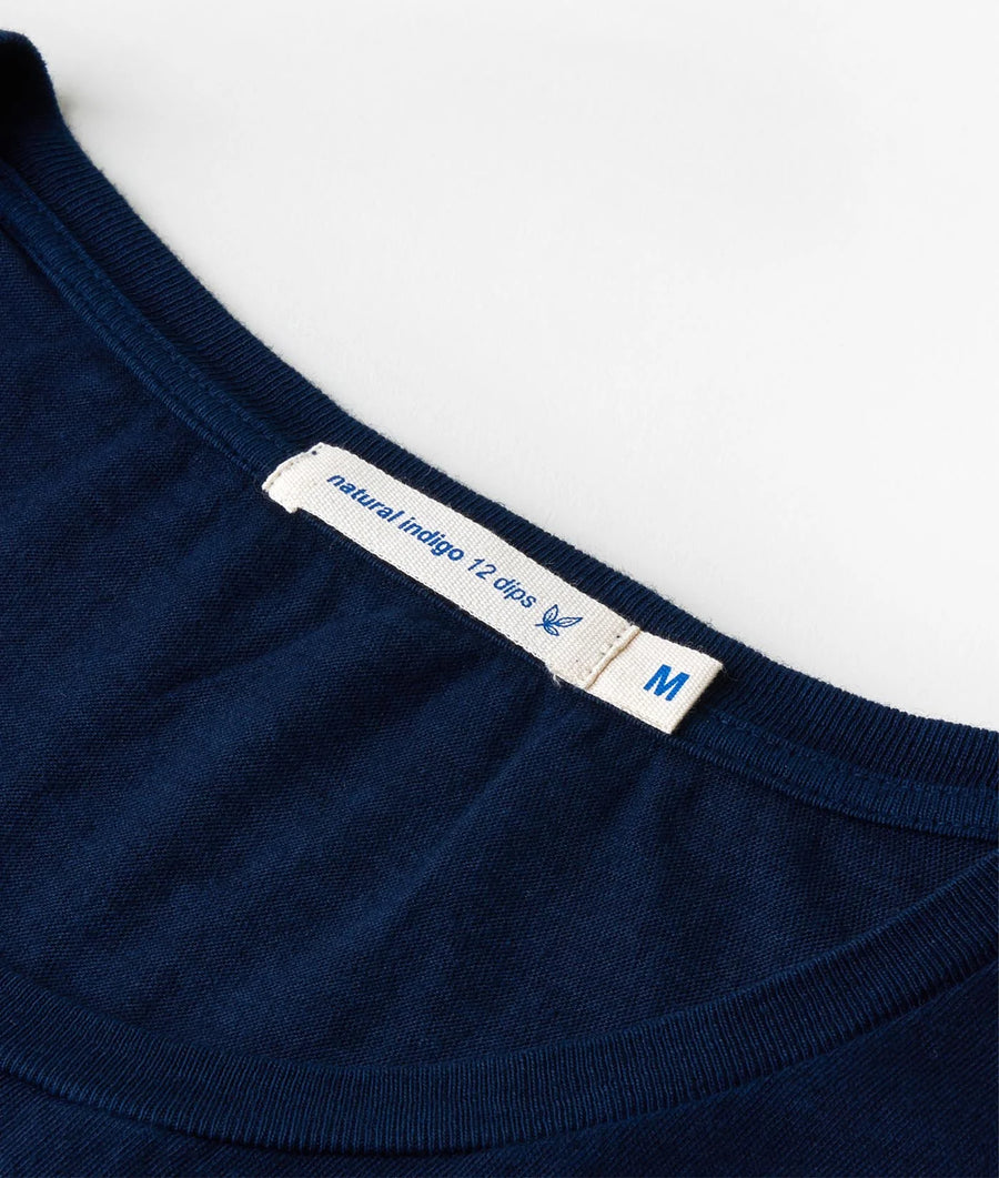A close-up detail shot of a navy blue ribbed cotton crew neck sweater, featuring the 'Natural Indigo 12 Clips' label - Industry of All Nations.