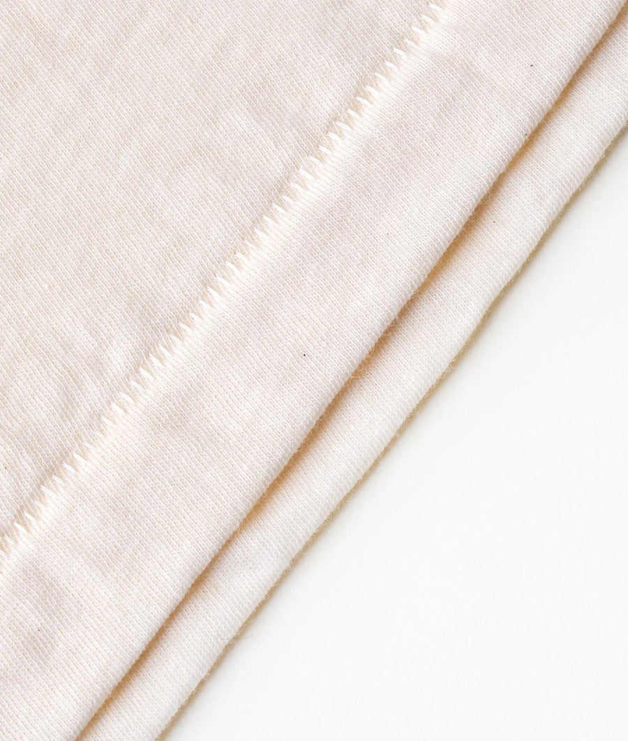 Flat lay image of a cream-colored knitted cotton textile with visible stitching detail - Industry of All Nations