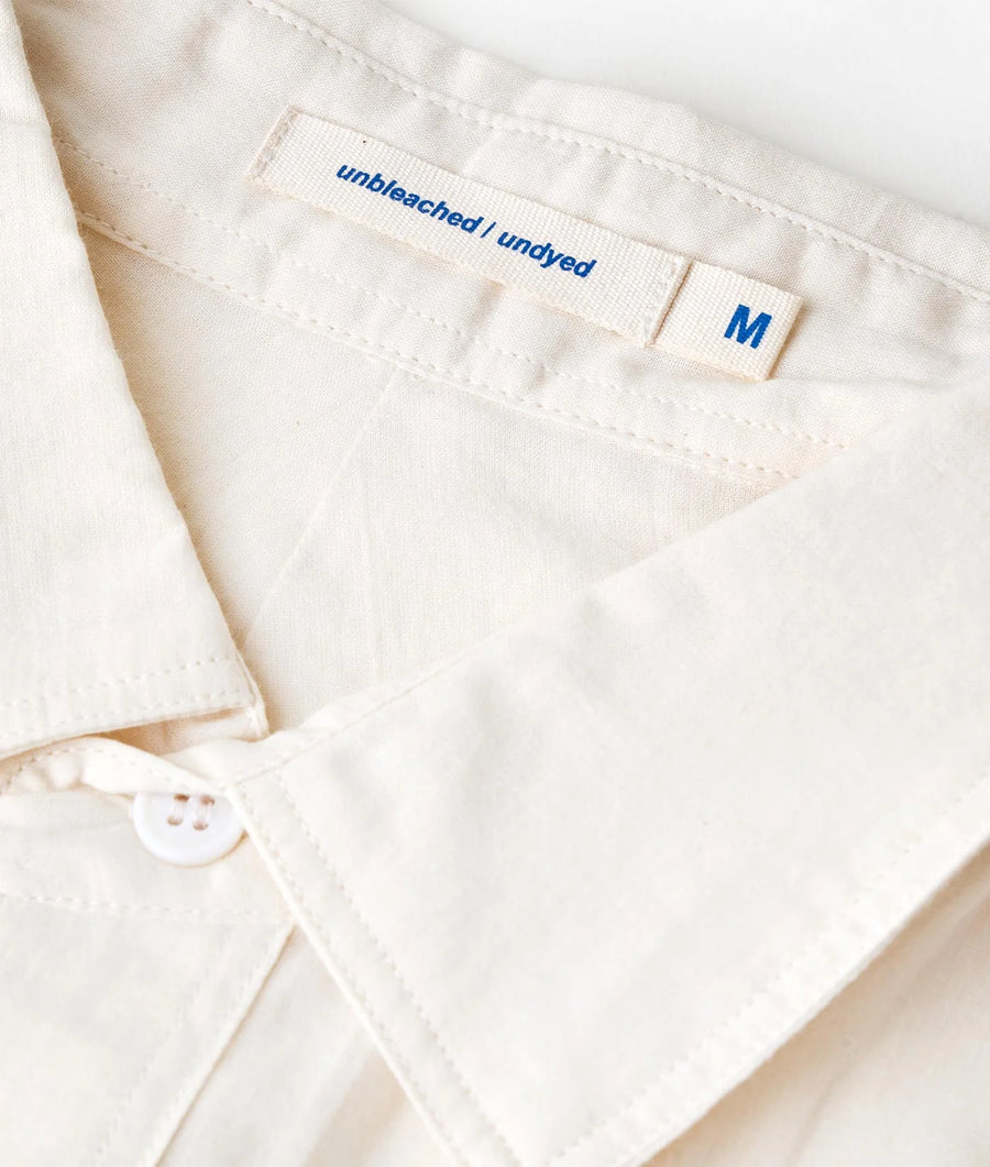 A close-up image of a white cotton shirt with "unbleached / undyed" label and "M" size indicator - Industry of All Nations