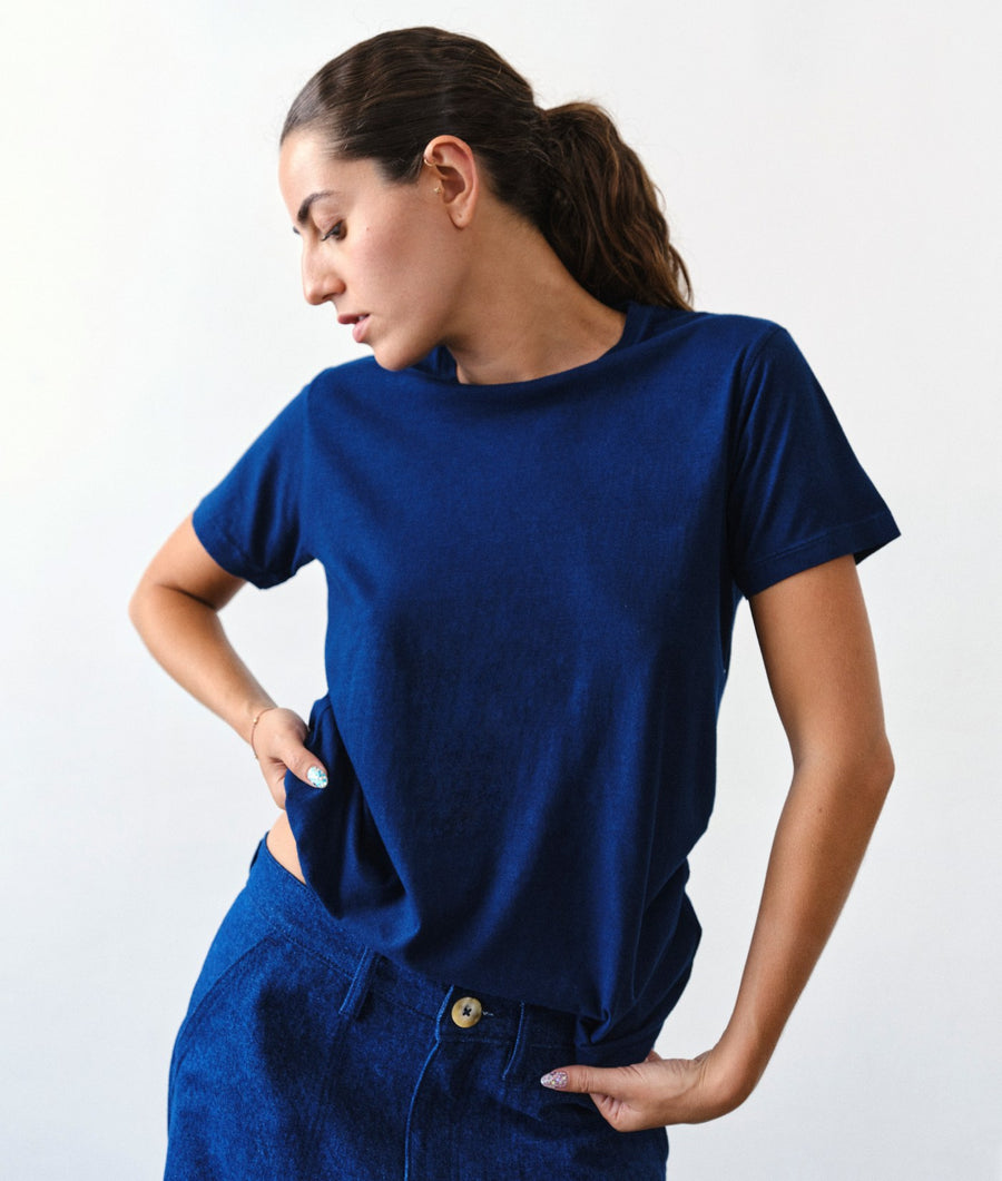 A woman wearing the IOAN Indigo 12 Short-Sleeve Crewneck T-Shirt with New Jeans pants, standing against a light gray studio background.