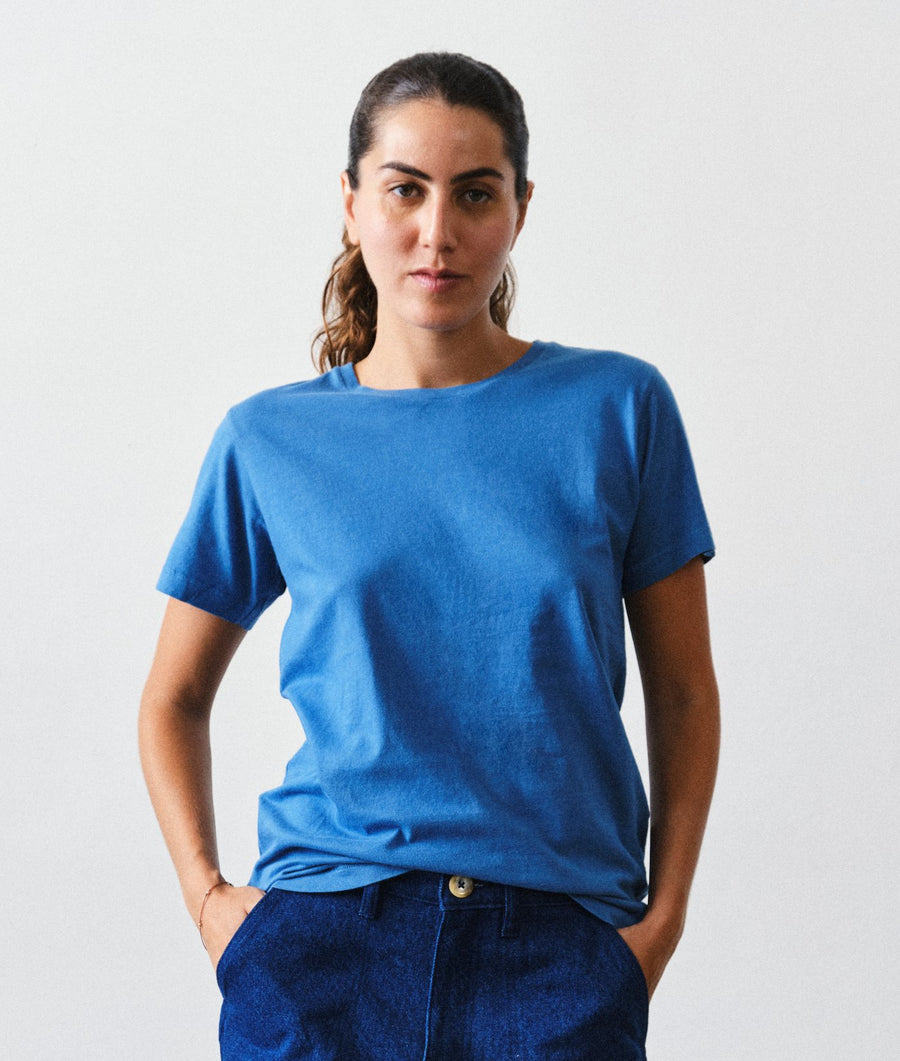 A woman wearing the IOAN Indigo 6 Short-Sleeve Crewneck T-Shirt with New Jeans pants, standing against a light gray studio background.