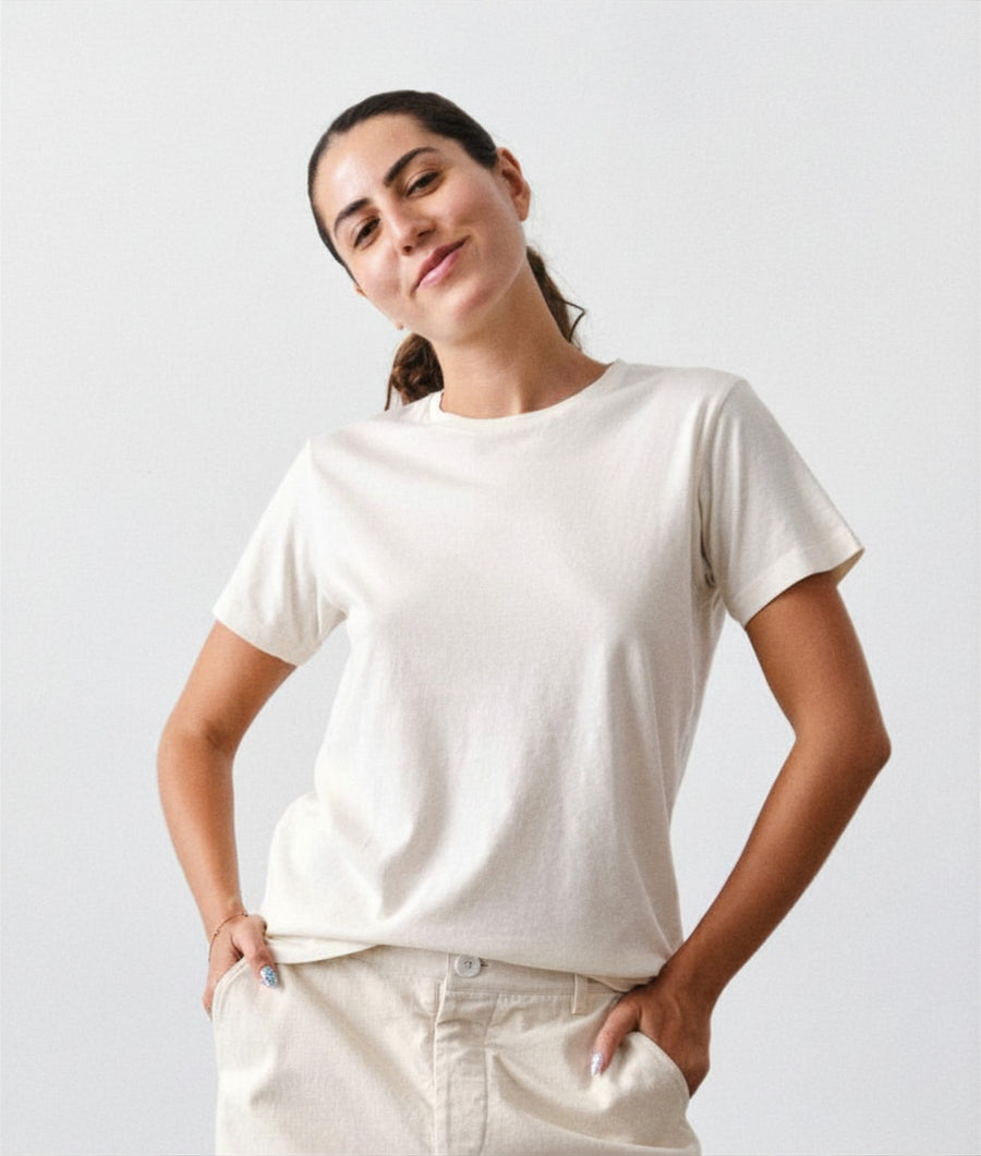 A woman wearing an IOAN Undyed Clean Crewneck T-shirt and Chinote Pants poses against a light gray studio background.
