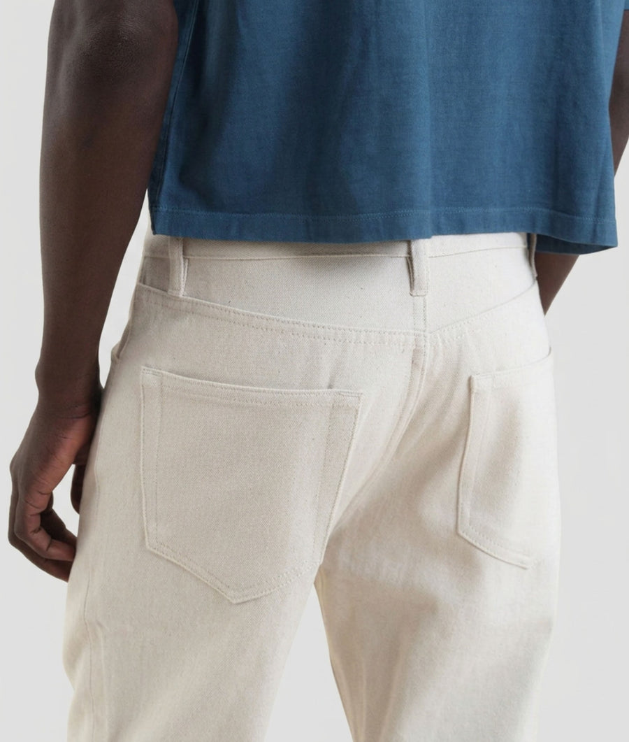 Close-up back view of a person wearing IOAN undyed pants with an Indigo 6 cropped t-shirt, showing the back pockets and waistband details against a light gray background.