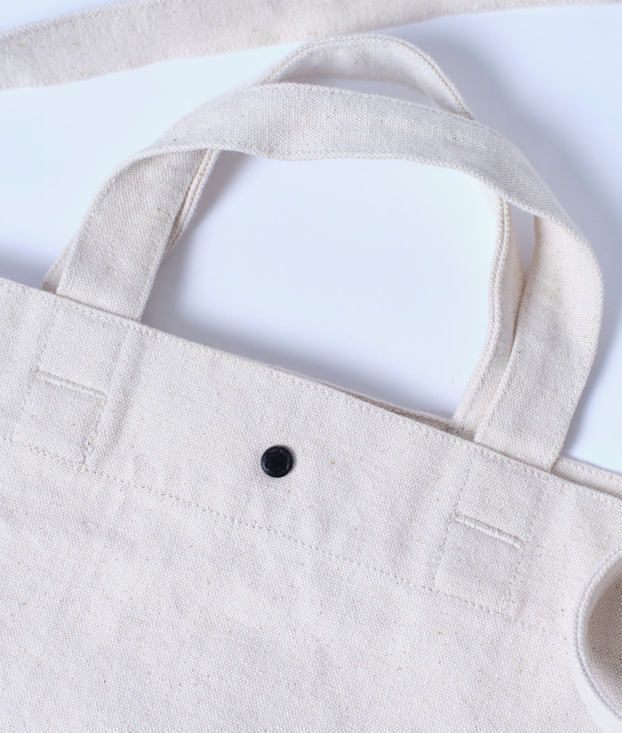 Beige cotton tote bag with black button detail, displayed in a flat lay - Industry of All Nations