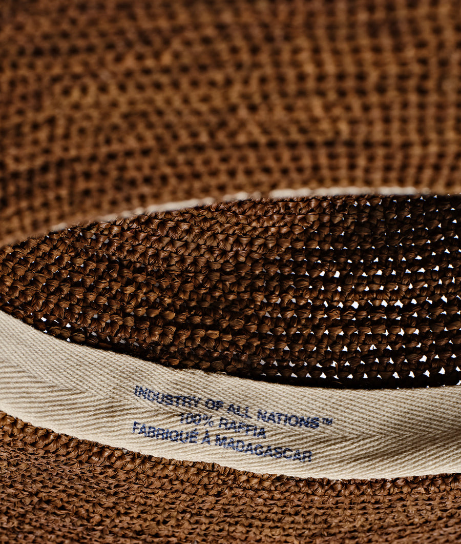 Detail shot of a woven brown hat with a fabric tag that says "Industry of All Nations" - Industry of All Nations