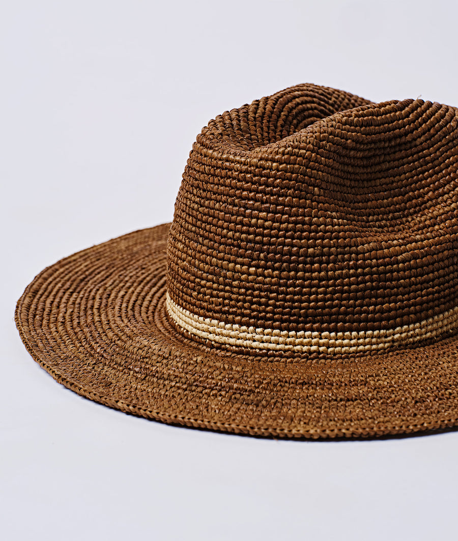 A close-up view of a woven straw sun hat in a warm brown color tone, displayed on a plain background - Industry of All Nations.