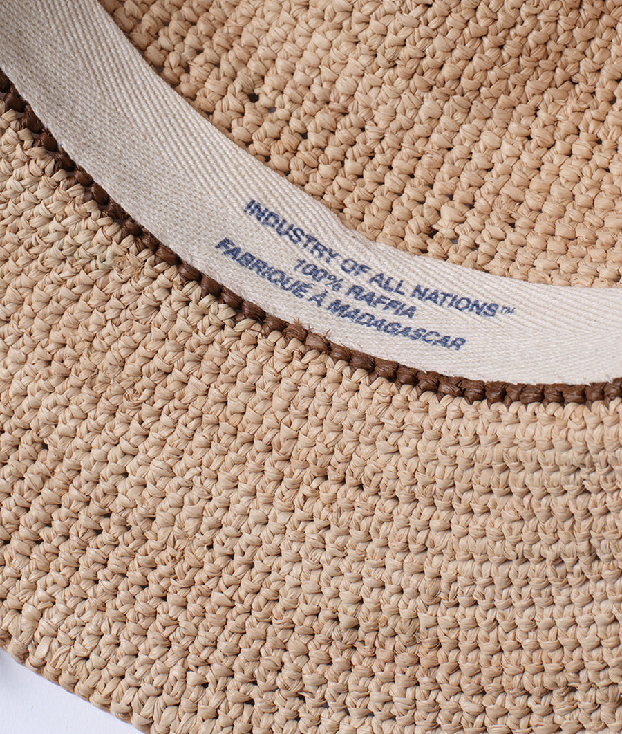 Detail shot of a tan, crocheted hat with "Industry of All Nations" logo - Industry of All Nations
