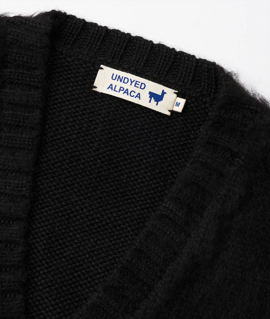 Detail shot of a black undyed alpaca fabric label on a textured, knit black fabric garment - Industry of All Nations