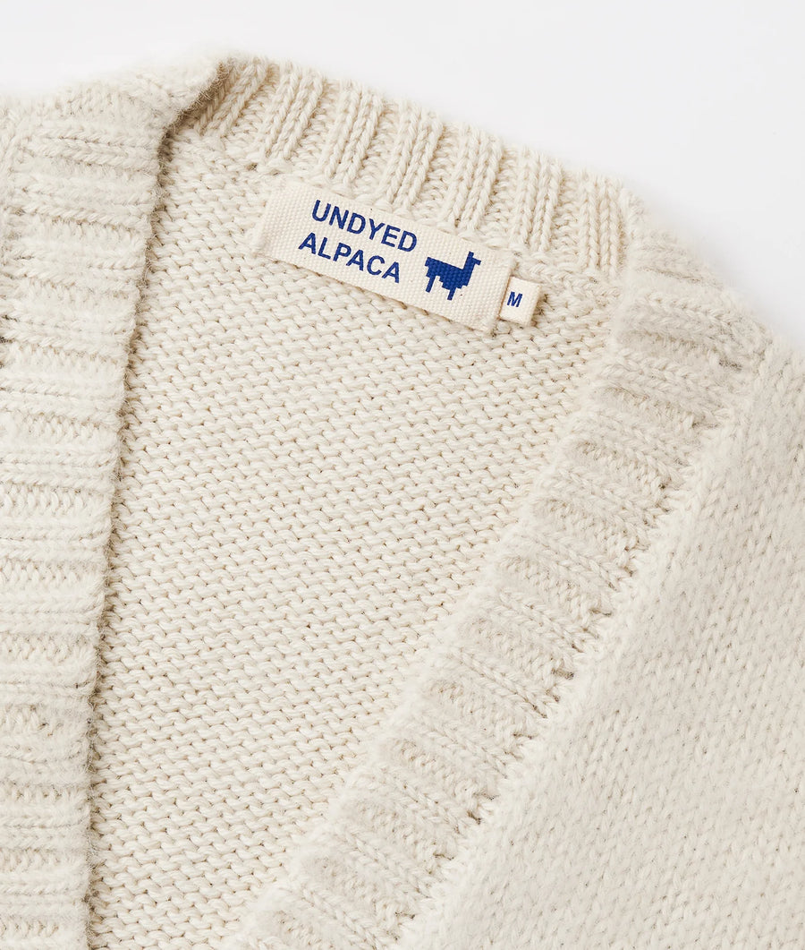 Flat lay detail shot of a cream-colored, ribbed knit alpaca sweater with a navy blue "Undyed Alpaca" label - Industry of All Nations