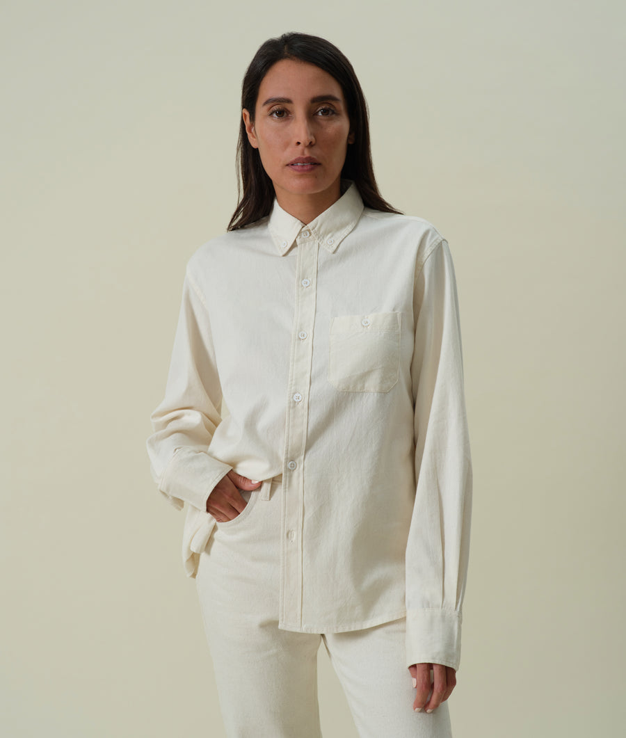 White button-down shirt worn by a woman with long dark hair, standing against a light background - Industry of All Nations
