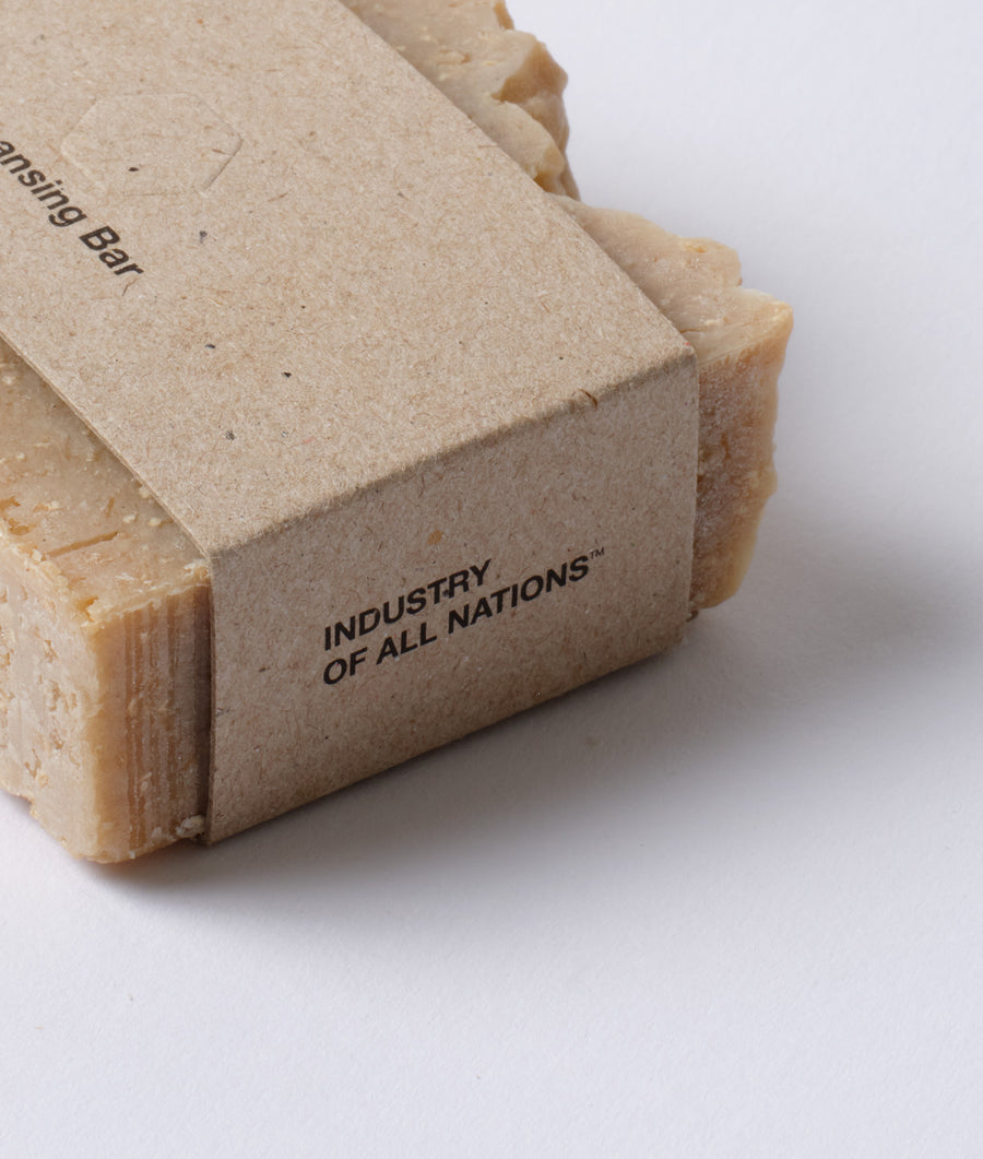 A close-up shot of a natural fiber bar soap with the "Industry of All Nations" branding displayed on the product packaging - Industry of All Nations