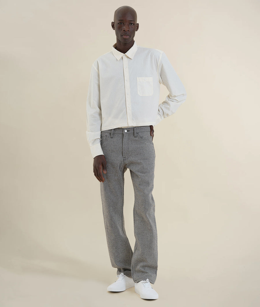 A man wearing a white collared shirt and gray straight-leg jeans standing in a neutral setting - Industry of All Nations