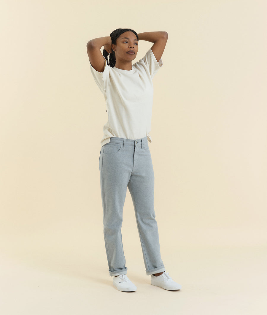 The person in the image is wearing a white t-shirt and light gray straight-leg pants while standing against a beige background - Industry of All Nations