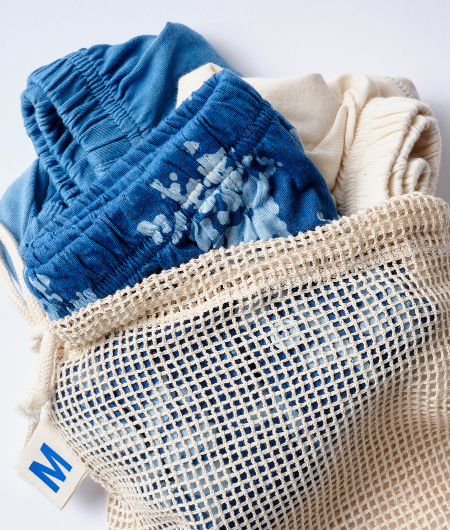 Flat lay of a blue printed organic cotton garment displayed in a mesh reusable bag - Industry of All Nations