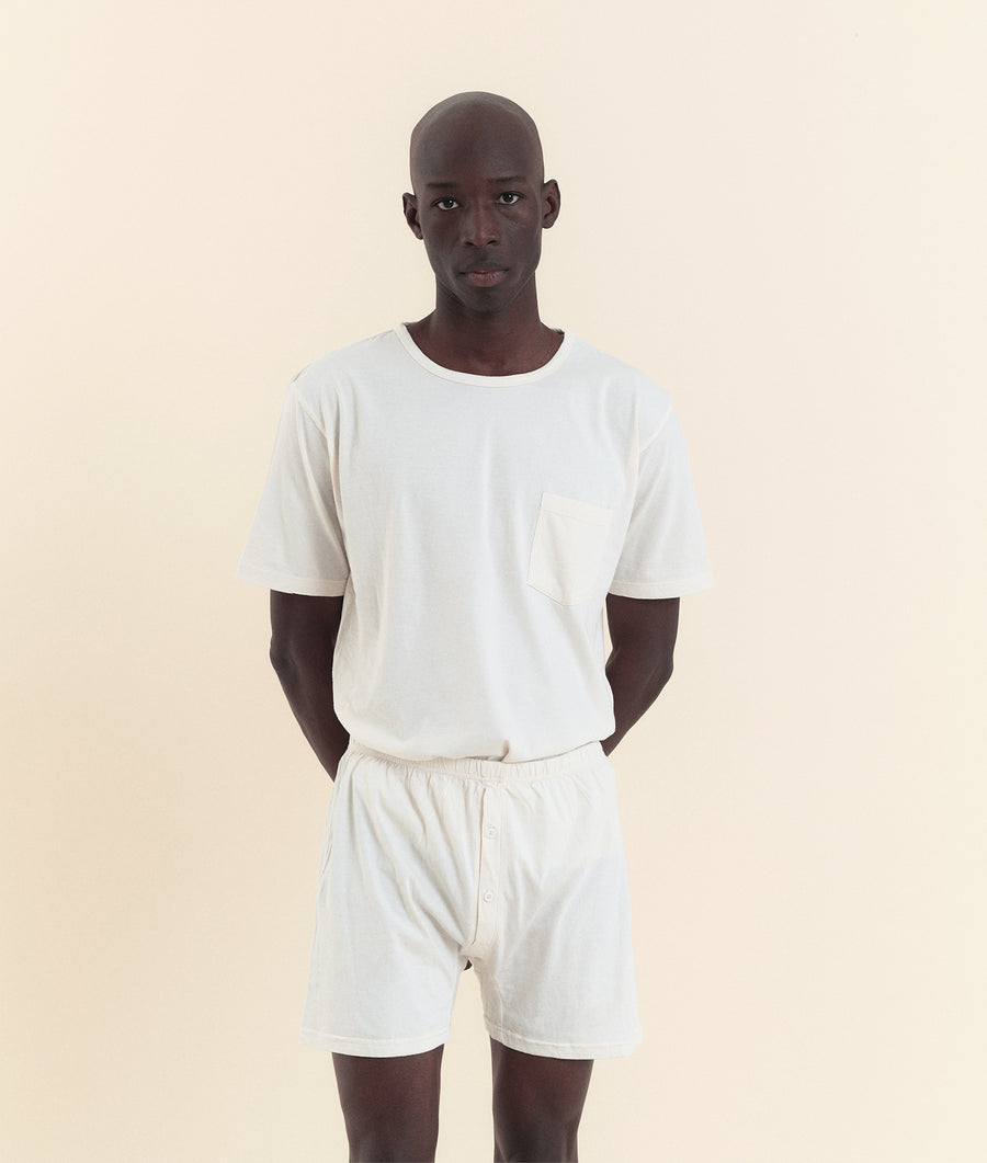 A young man wearing a white cotton t-shirt and shorts, standing against a light background - Industry of All Nations