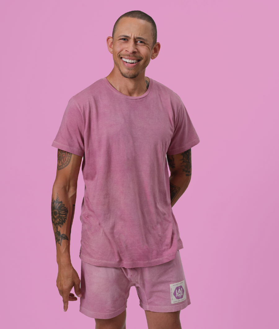 A smiling man wearing a pink t-shirt and matching shorts against a pink background - Industry of All Nations