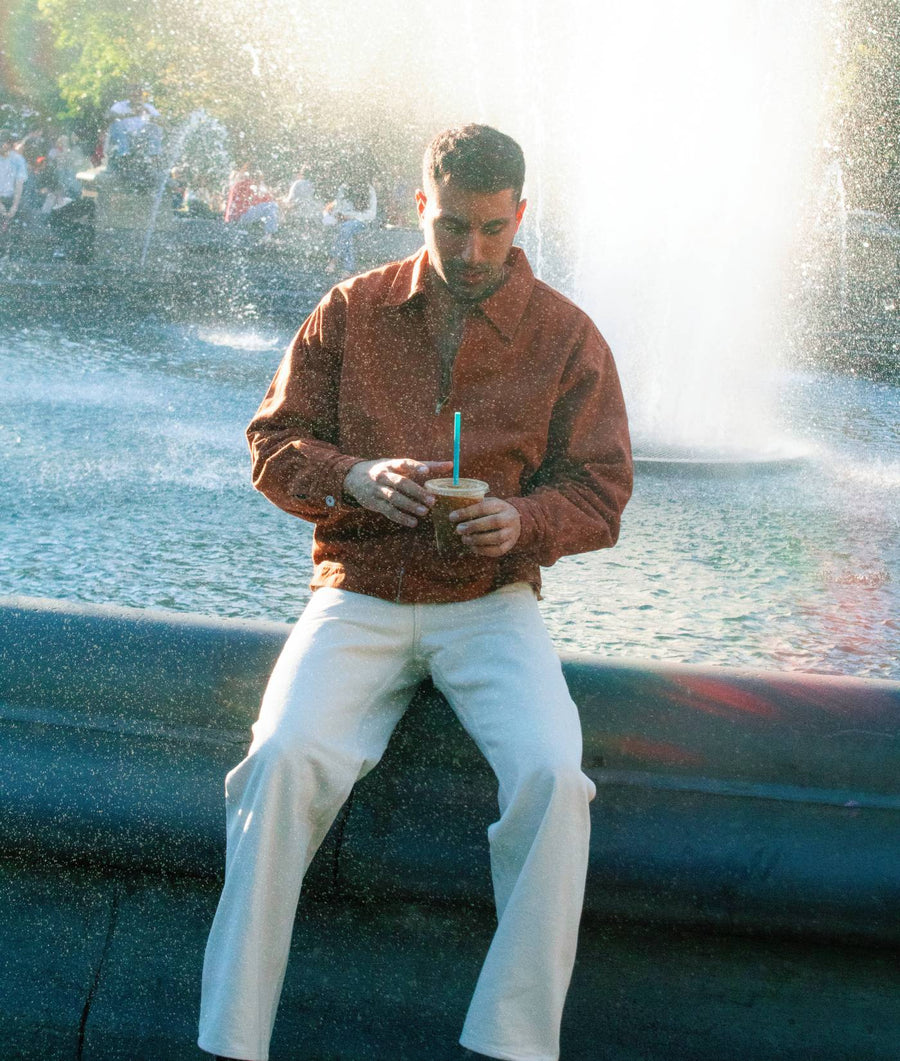 A person wearing a rust-colored, button-up shirt in front of a water fountain - Industry of All Nations