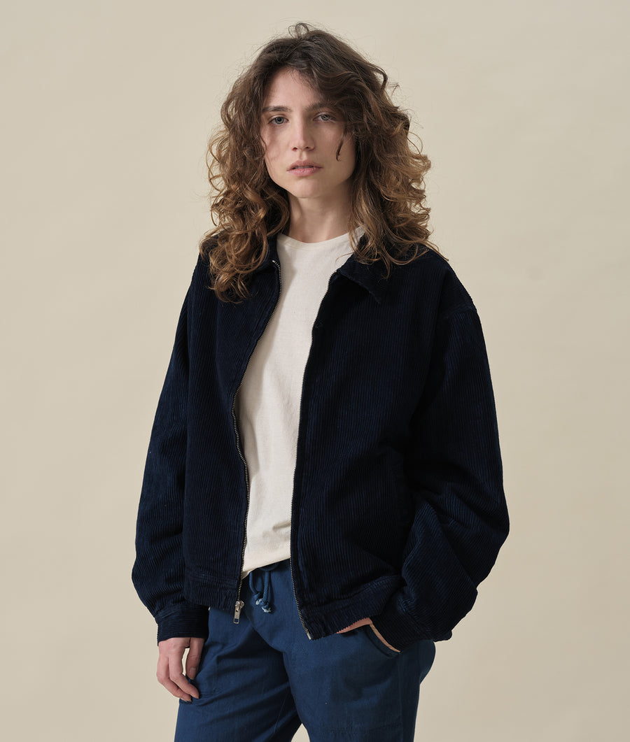 A young woman wearing a black ribbed zip-up jacket over a white sweater - Industry of All Nations