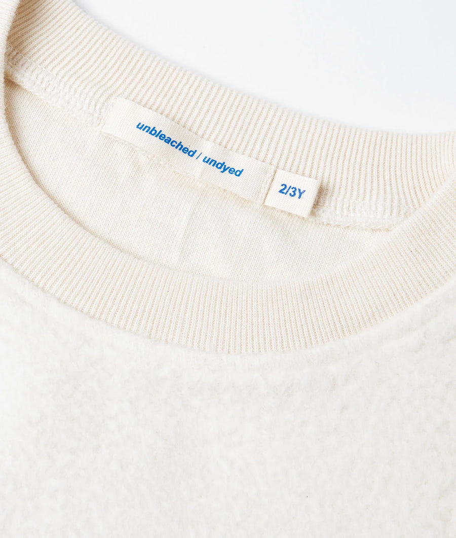 A closeup detail shot of the fabric and care label on a beige unbleached/undyed cotton garment made by Industry of All Nations.