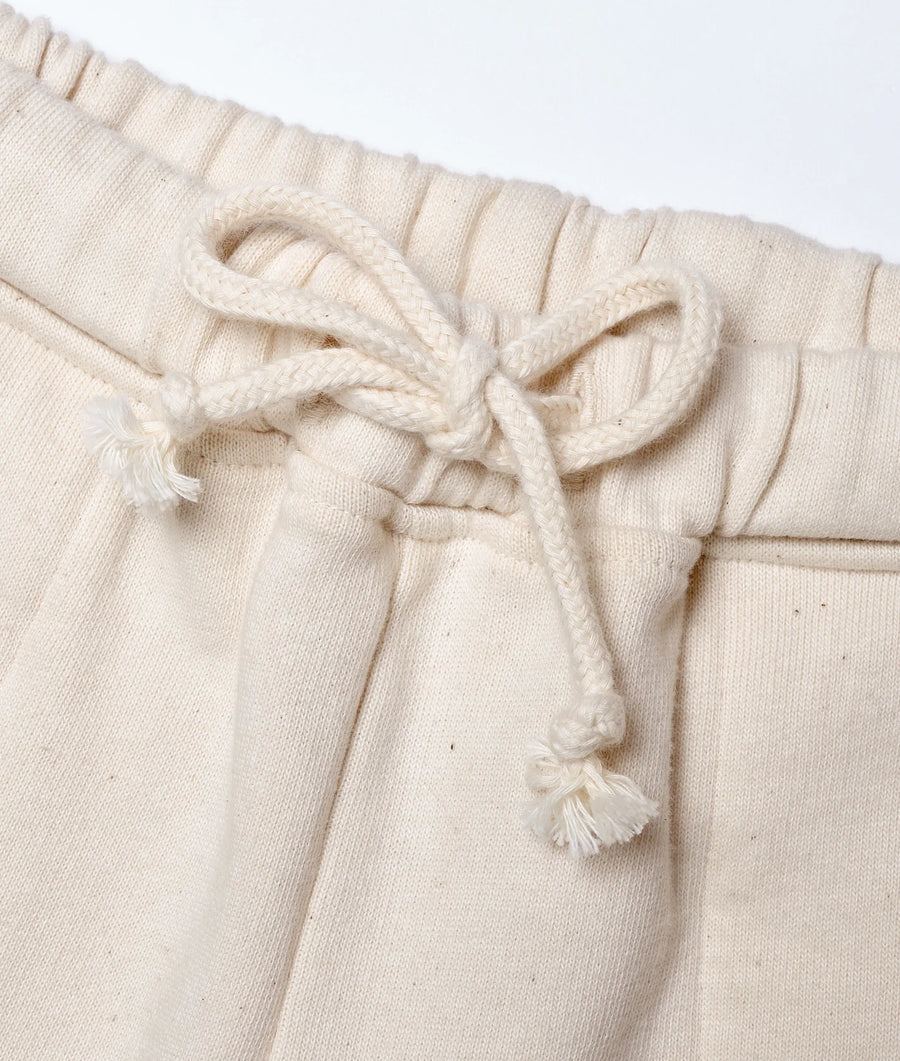 A detail shot of a beige, knitted cotton garment with a drawstring waist and tasseled tie - Industry of All Nations
