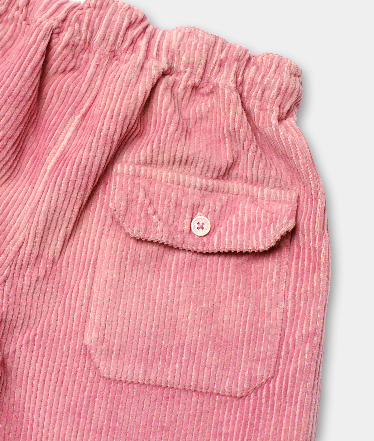 Detailed close-up of a pink pleated corduroy shirt with a button closure - Industry of All Nations