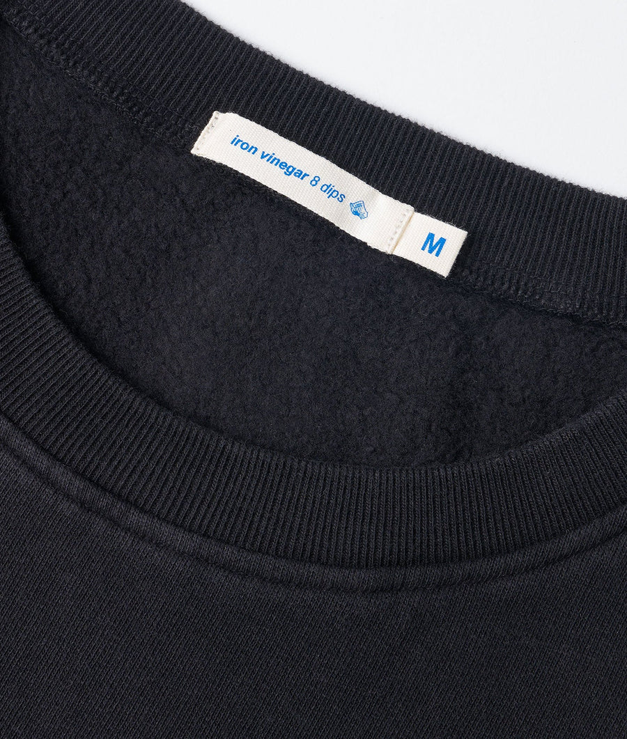 A close-up detail shot of the neck and sizing tag on a black iron vinegar & dips crewneck sweater from Industry of All Nations.