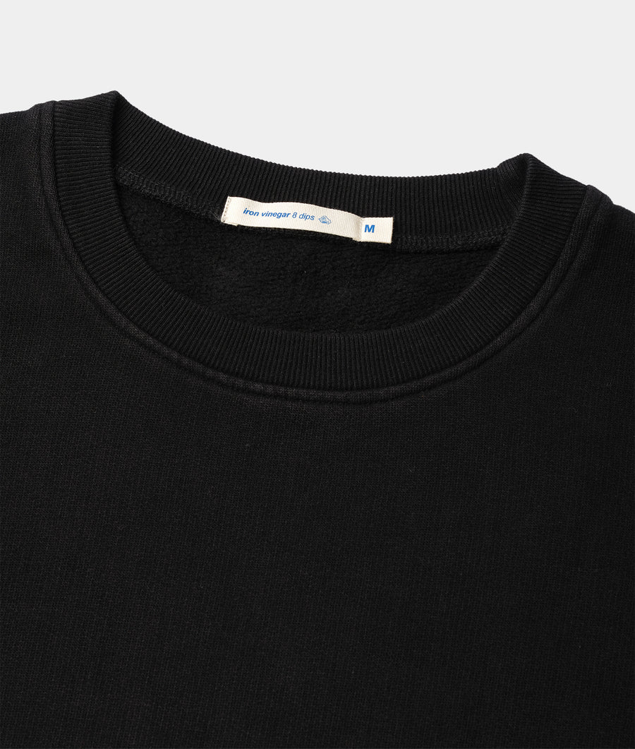 A close-up detail shot of a black, ribbed crewneck sweater from Industry of All Nations.