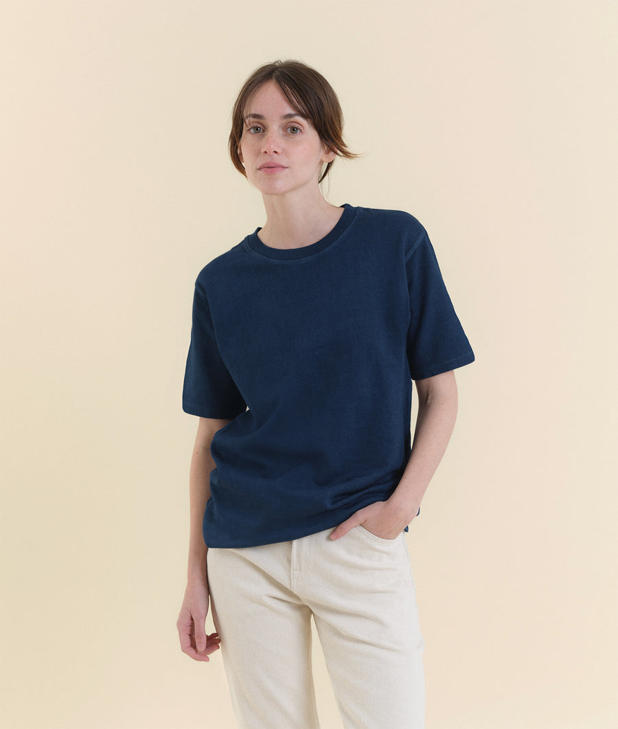The image shows a woman wearing a navy blue short-sleeved t-shirt against a light cream background - Industry of All Nations