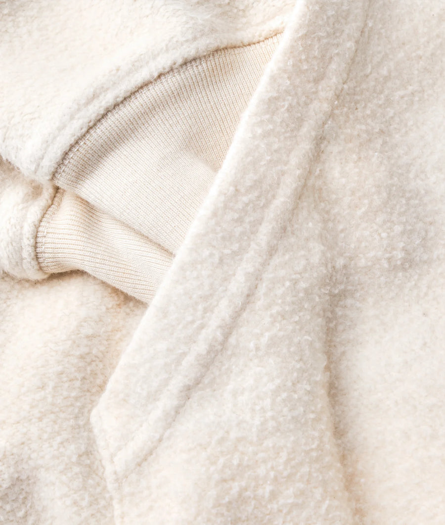 A close-up image of a soft, beige wool sweater with a ribbed knit collar and cuffs - Industry of All Nations