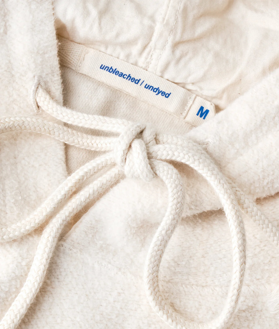 Detail shot of a white, medium-sized unbleached/undyed bathrobe with a tie closure, displaying the label - Industry of All Nations.