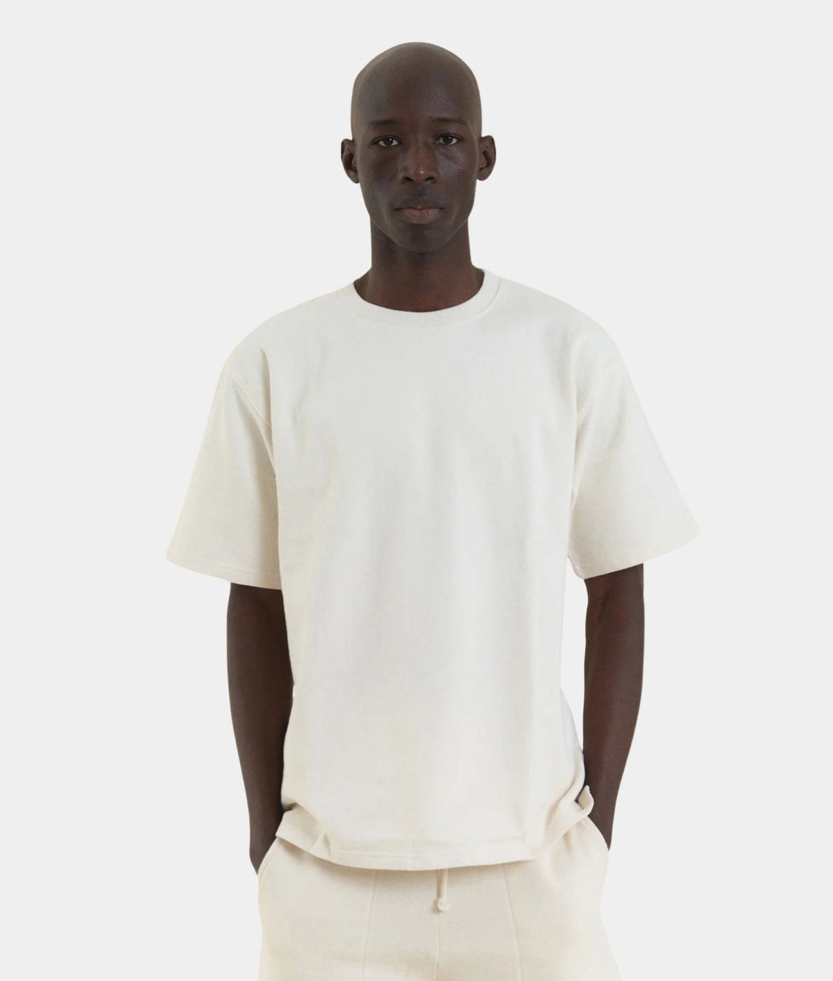 A man wearing an undyed IOAN Kung Fu T-shirt with matching off-white pants, standing against a light gray background.