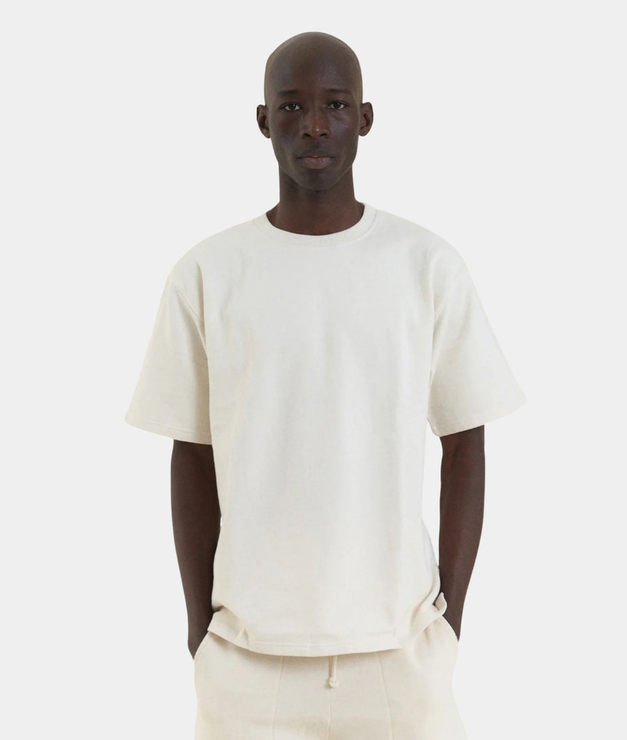 A man wearing an undyed IOAN Kung Fu T-shirt with matching off-white pants, standing against a light gray background.