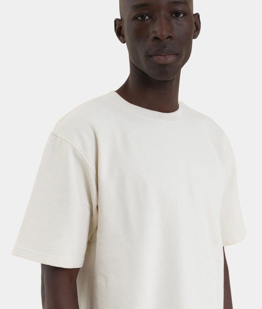 A man wearing an undyed IOAN Kung Fu T-shirt with matching off-white pants, standing against a light gray background.