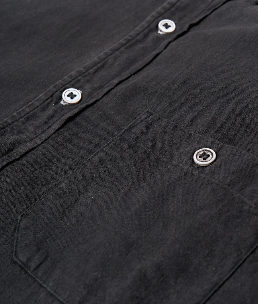 Detail shot of a black organic cotton shirt with white buttons from Industry of All Nations.
