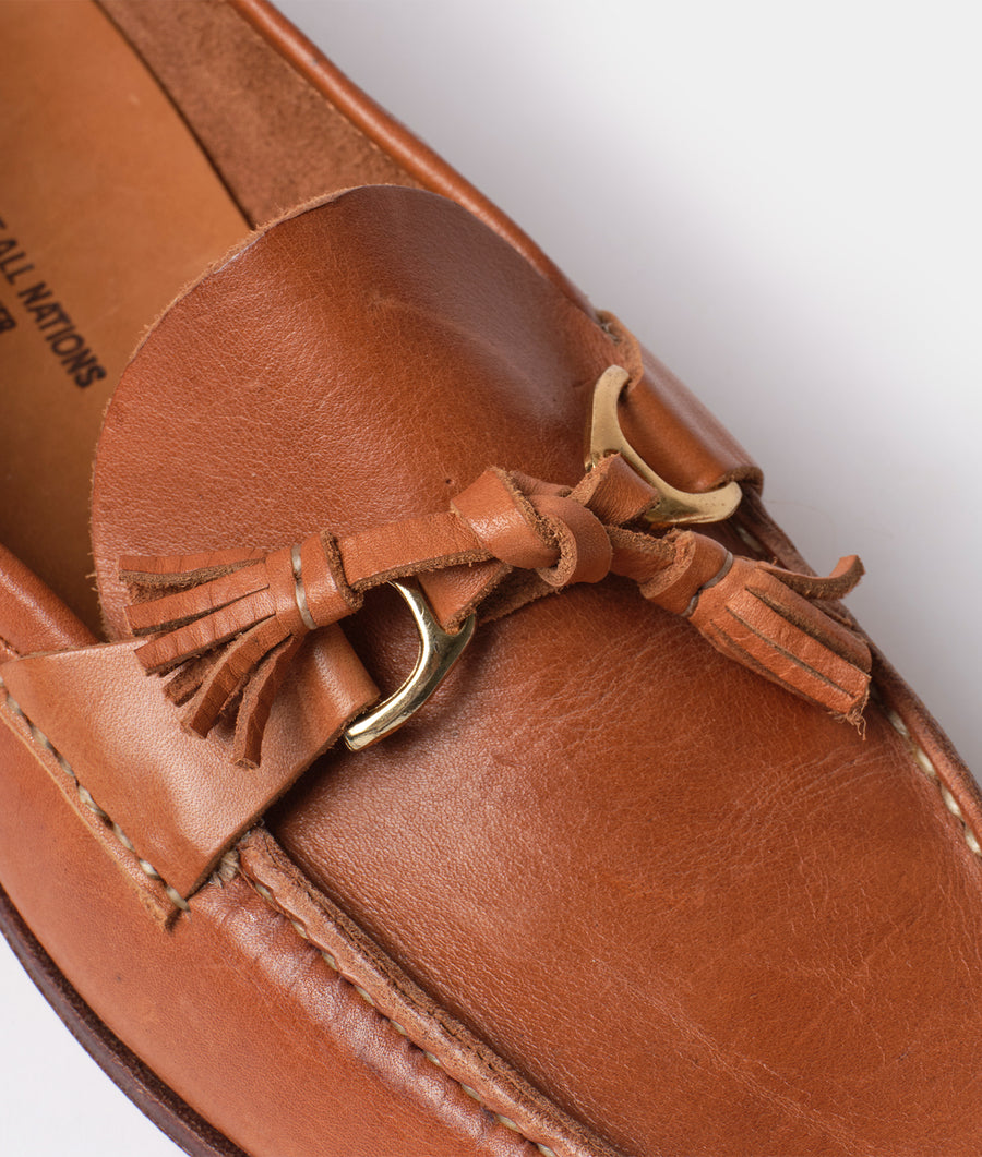 Closeup of a brown leather moccasin with fringes and a brass clasp fastener - Industry of All Nations