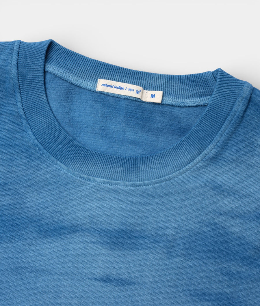 Close-up detail shot of a blue crew neck t-shirt with ribbed trim, label showing "natural indigo 2 dips" - Industry of All Nations