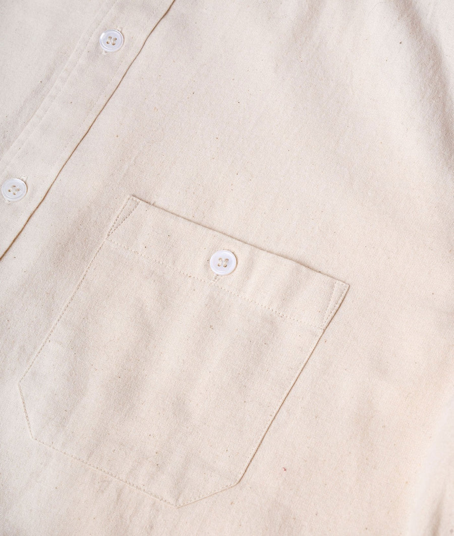 Detail shot of a beige organic cotton shirt featuring white buttons and a front pocket - Industry of All Nations