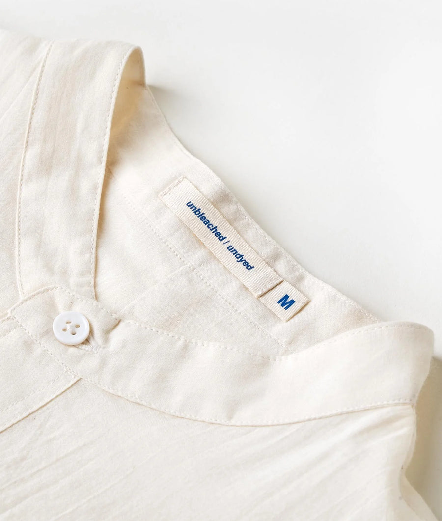 Flat lay detail shot of a white organic cotton button-down shirt with "unbleached and undyed" text tag - Industry of All Nations