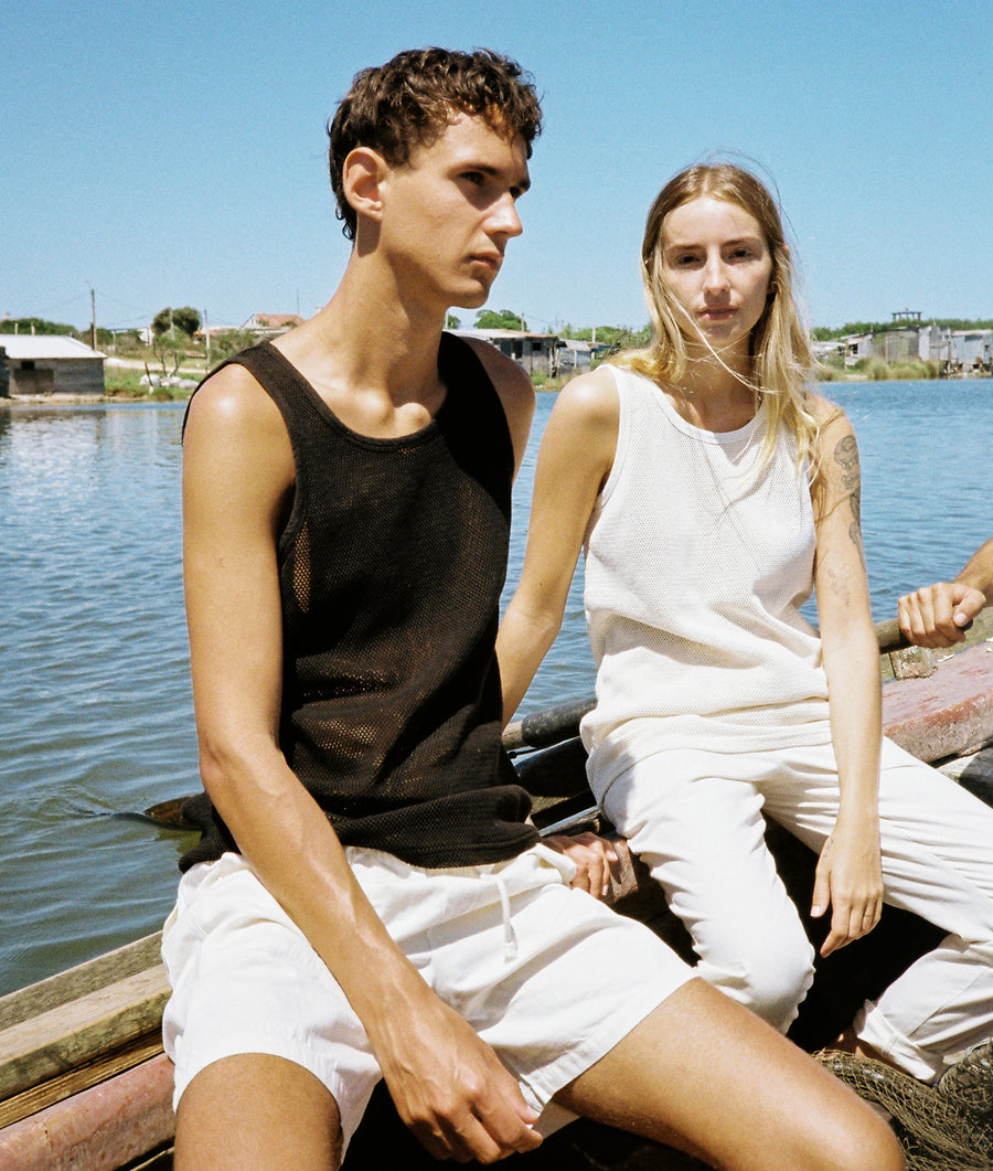 A man and woman wearing casual, lightweight clothing sitting by a body of water - Industry of All Nations.