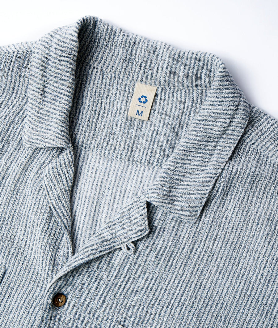 A gray and white striped knitted sweater displayed as a flat lay, showing the recycling logo on the label - Industry of All Nations