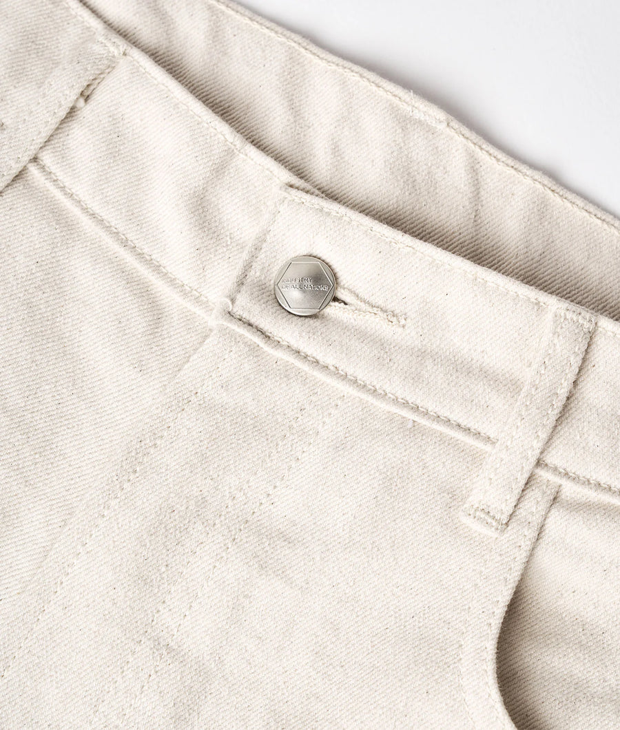 A close-up detail shot of a light beige, organic cotton garment with a metal button fastener - Industry of All Nations