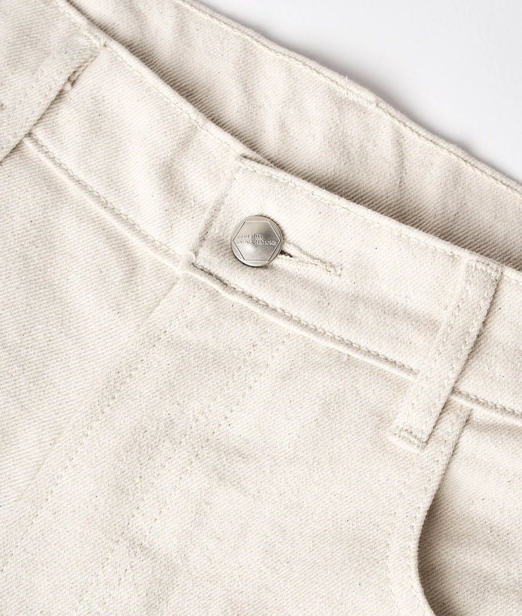 A close-up detail shot of a light beige, organic cotton garment with a metal button fastener - Industry of All Nations