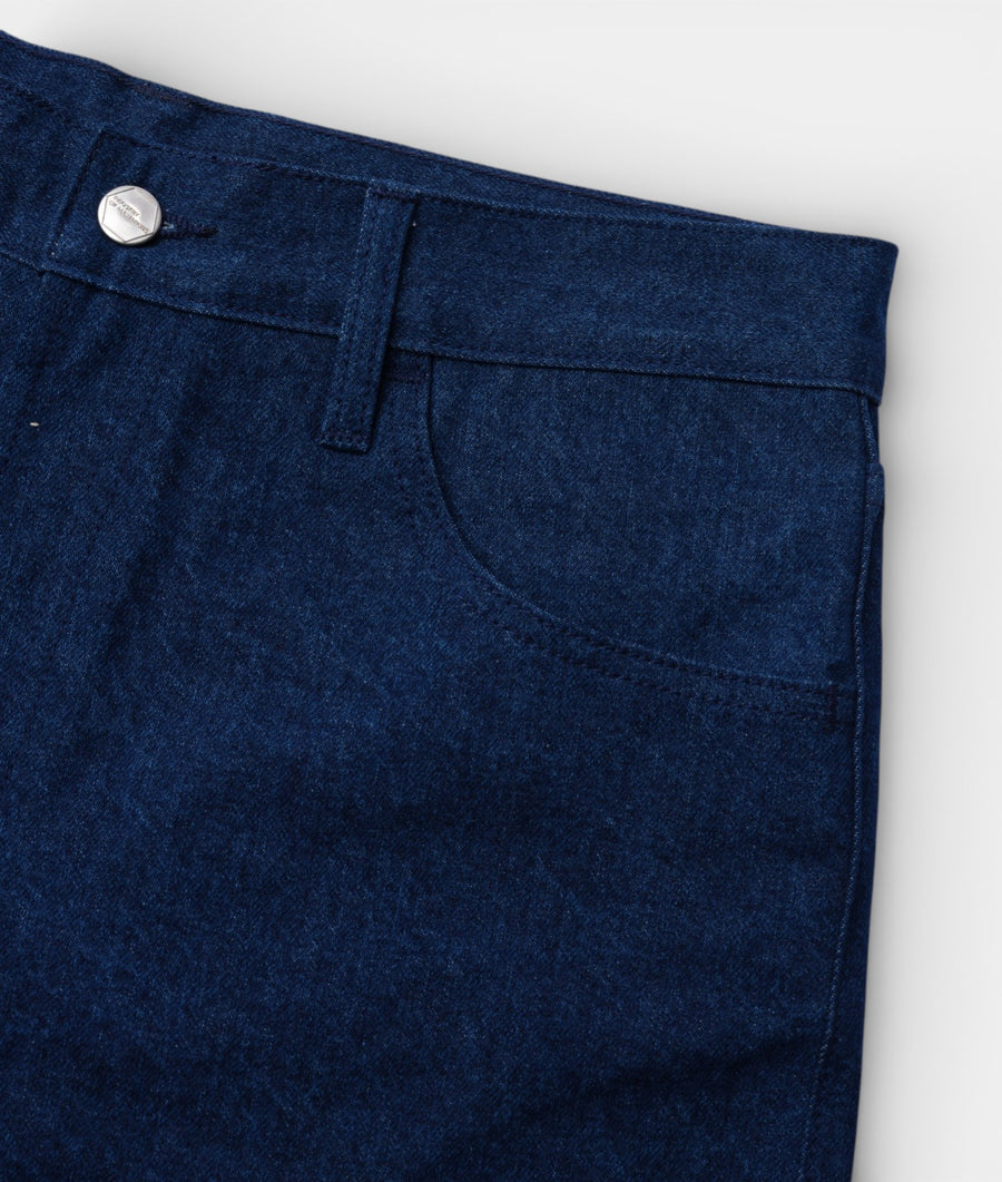 Close-up image of a dark blue organic cotton denim pant laid flat with visible stitching and zipper detail - Industry of All Nations