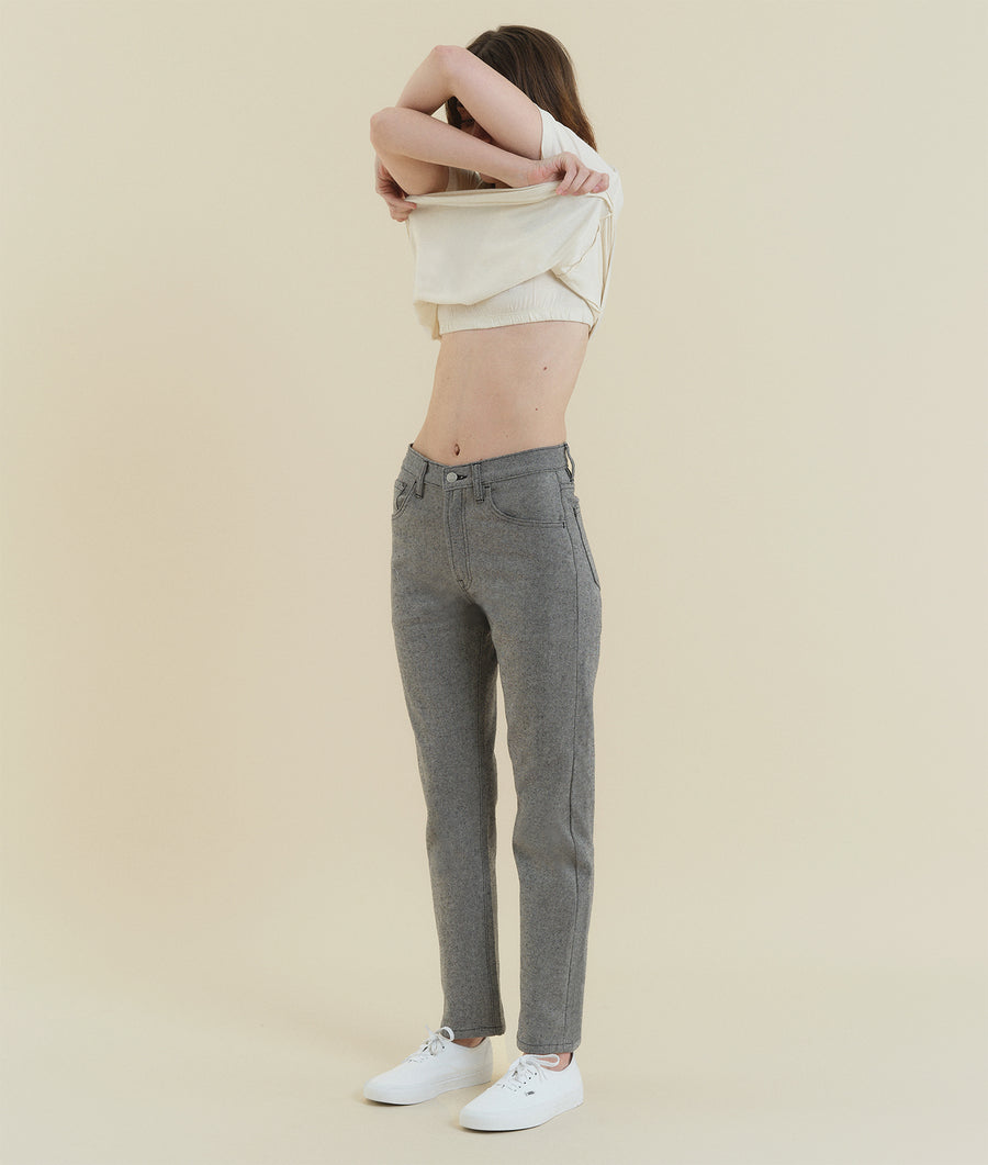 A young woman wearing a white cropped top and grey high-waisted pants, standing against a beige background - Industry of All Nations