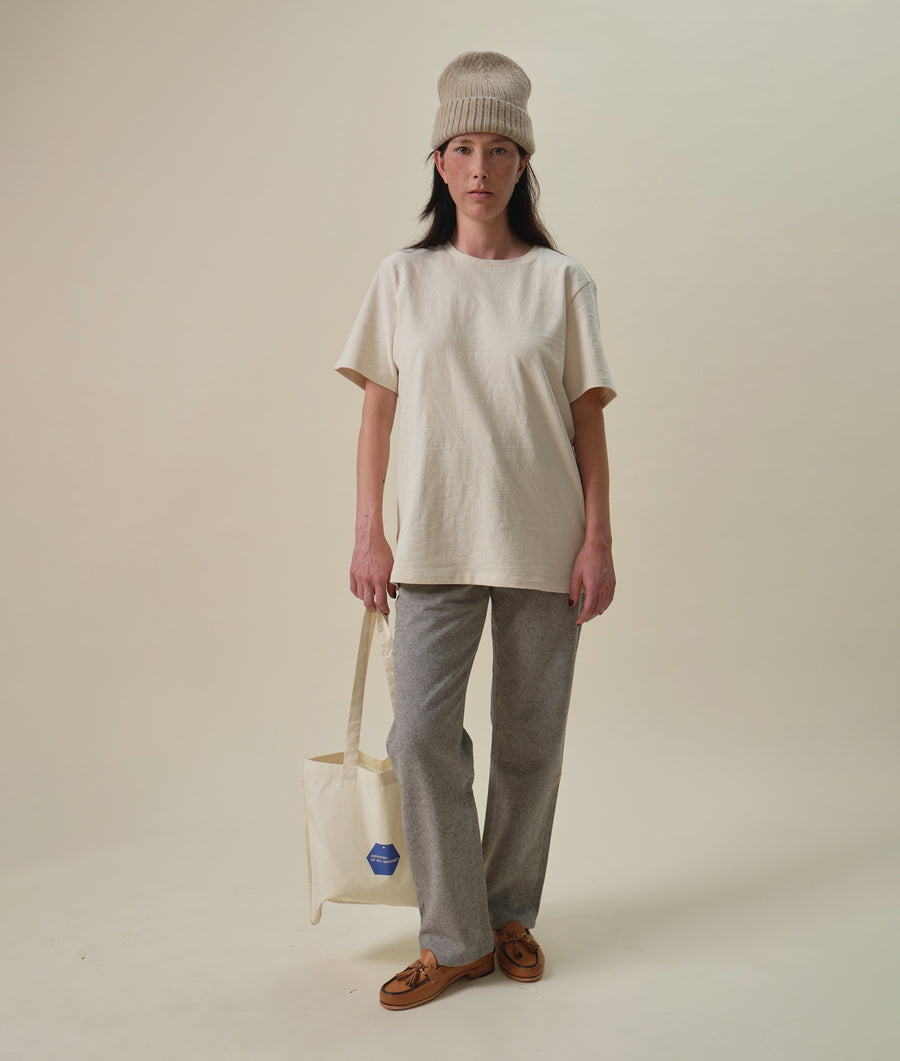 A model wearing a cream colored short sleeve t-shirt and grey sweatpants, holding a canvas tote bag - Industry of All Nations