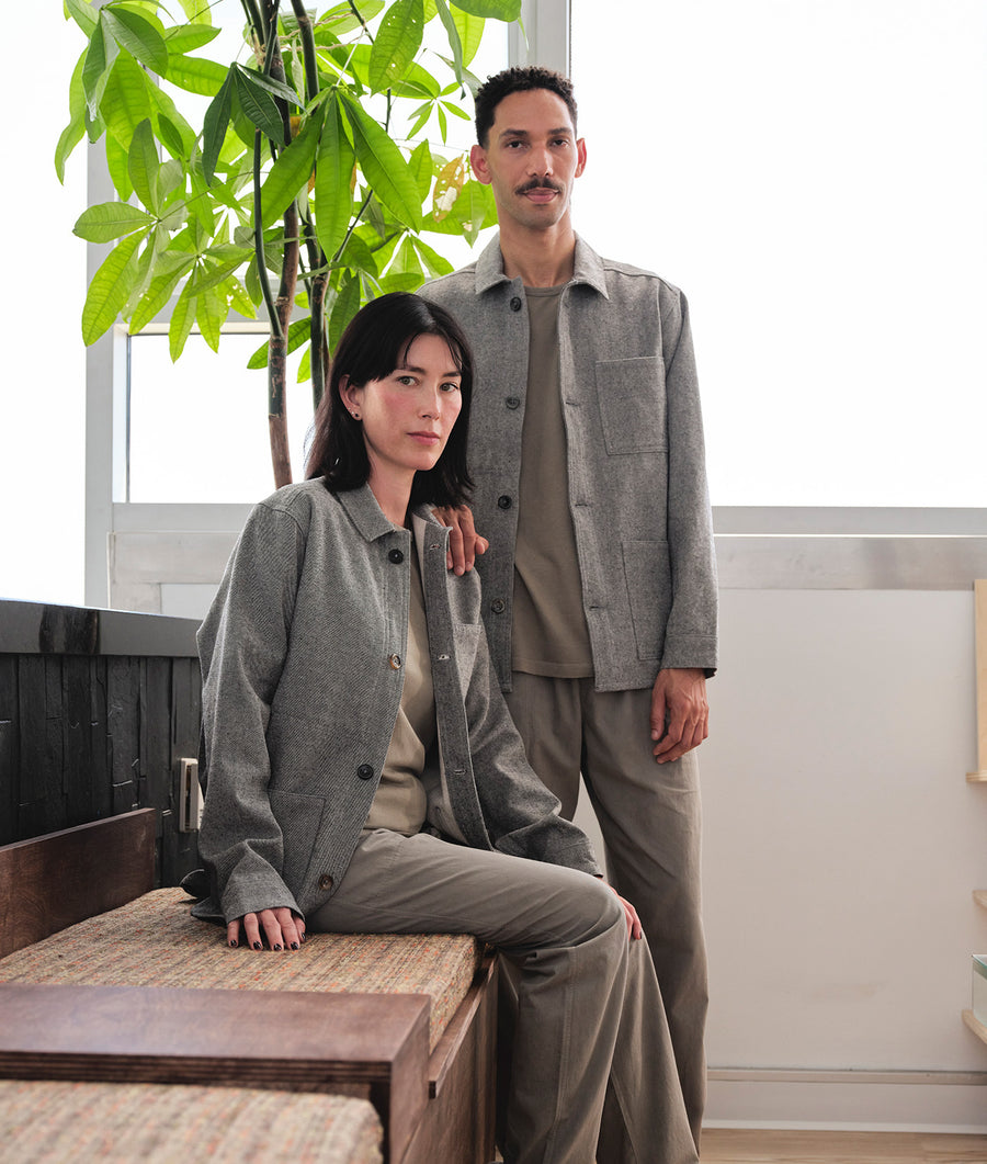 Two people wearing gray wool outerwear and matching pants, standing in a room with potted plants - Industry of All Nations